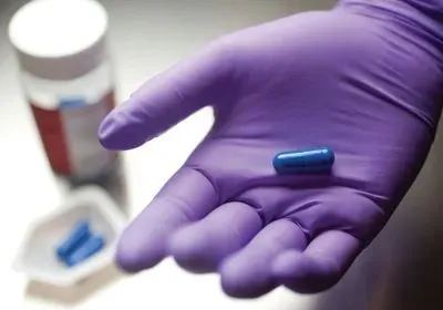 A person wearing a purple glove holds out a blue pill